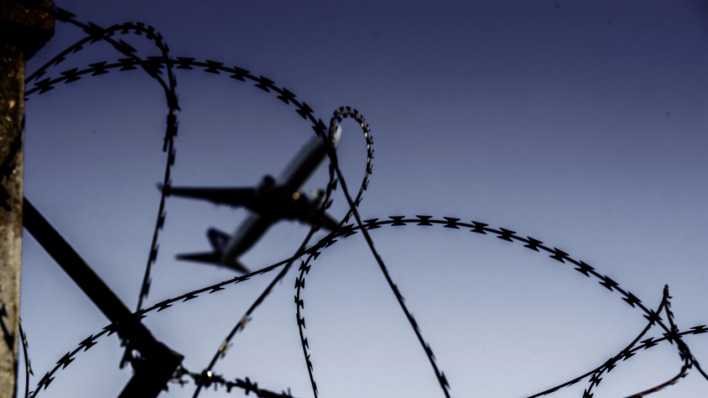 Ein Flugzeug fliegt hinter Stacheldraht (Bild: picture alliance/Robert Schlesinger)