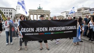 Teilnehmende einer Demonstration halten vor dem Brandenburger Tor ein Banner mit der Aufschrift "Gegen jeden Antisemitismus" hoch.