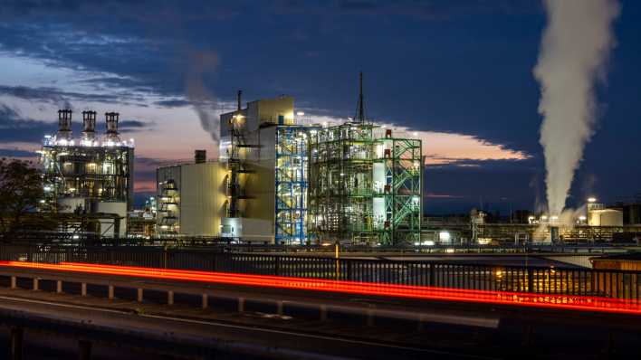 Dampf und Rauch steigen aus einer Industrieanlage im Chemiepark Wesseling im Vordergrund sind die vorbeiziehenden Rücklichter eines Autos zu sehen.