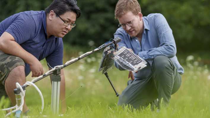 Zwei Forscher testen ihren Prototyp für ein Roboterbeinauf einer Wiese.