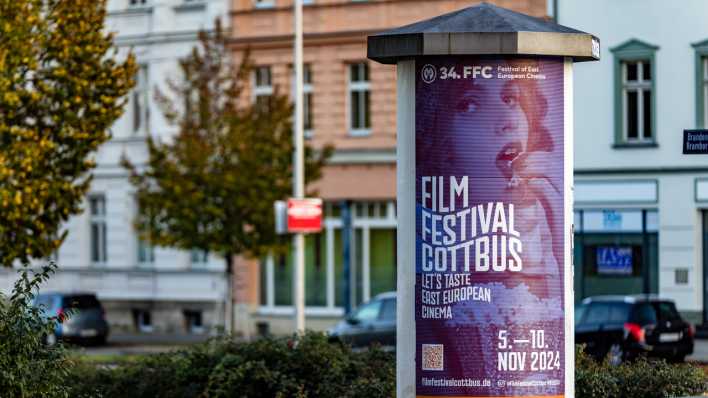 Eine Litfaßsäule mit einem Werbeplakat für das Cottbuser Filmfestival steht an einer Innenstadtkreuzung.