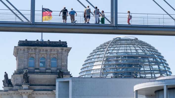 Menschen stehen auf dem Marie-Elisabeth-Lüders-Steg im Berliner Regierungsviertel und blicken auf das Reichstagsgebäude.