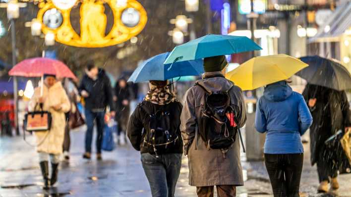 Passanten gehen mit Regenschirmen über eine Einkaufsstraße in Essen.