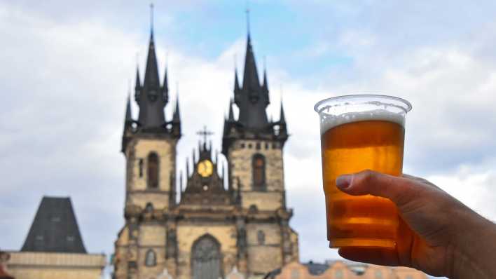 Eine Person hält einen Bierbecher vor der Prager Teynkirche (Foto: imago images / Panthermedia)