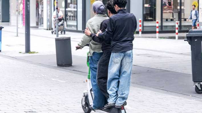 Drei Jugendliche auf einem E-Scooter