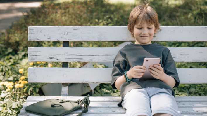 Lächelnder Junge mit Smartphone auf einer Bank