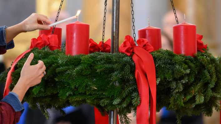 Eine Frau zündet die erste Kerze an einem Adventskranz an.