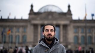 Tareq Alaows steht vor dem Reichstagsgebäude in Berlin.