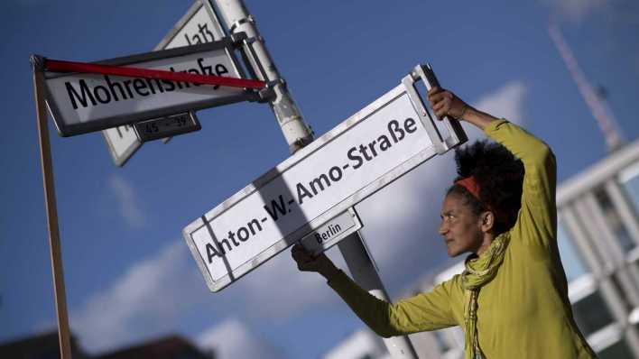 ARCHIV, Berlin, 23.08.2017: Frau protestiert mit Strassenschild "Anton-W.-Amo-Strasse" als neuen Namensgeber in Erinnerung an den ersten deutschen schwarzen Akademiker Anton Wolhelm Amo (Bild: IMAGO/IMAGO)