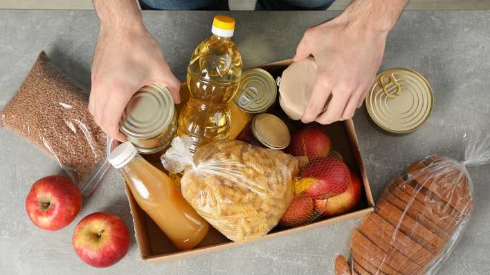 Ein Mann packt Lebensmittel wie Öl, Brot und Äpfel in eine Box.