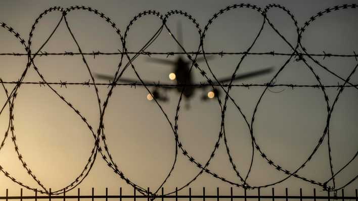 Ein Stacheldrahtzaun am Flughafen Düsseldorf - mit einem Flugzeug im Hintergrund.