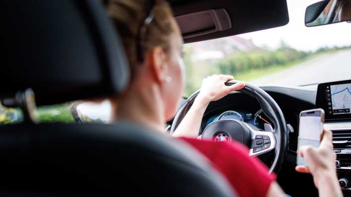 Eine Frau sitzt hinter dem Lenkrad eines Autos und benutzt ihr Handy.