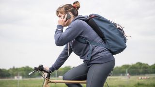 Eine Frau fährt mit dem Fahrrad auf dem Tempelhofer Feld in Berlin und telefoniert mit einem Smartphone (gestellte Szene).