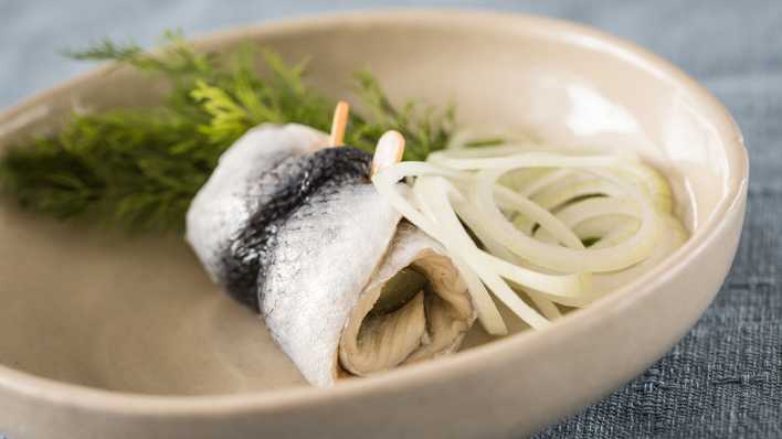 Ein Rollmops mit Zwiebeln auf einem Teller.