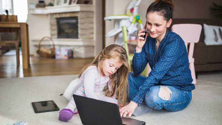 Frau, die mit ihrer Tochter zusammensitzt und mit dem Handy spricht (Bild: picture alliance / imageBROKER / Oleksandr Latkun)