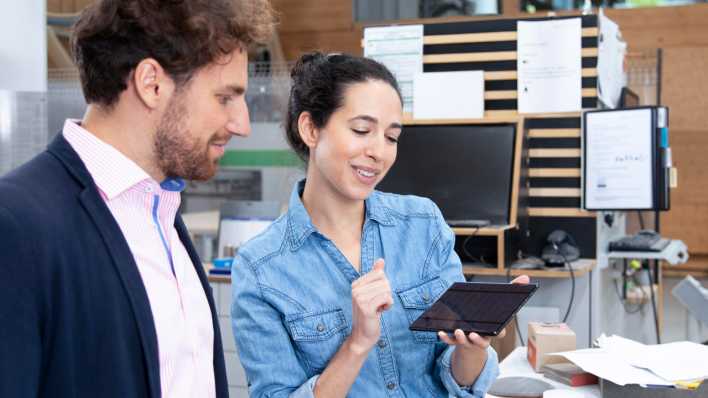 Symbolbild: Startup. Eine junge Frau zeigt einem jungen Mann in einem Büro etwas auf einem Tablet. (Bild: picture alliance / Westend61 / Florian Küttler)