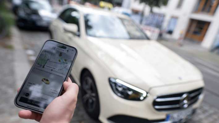 Smartphone mit Uber-App geöffnet vor Taxi