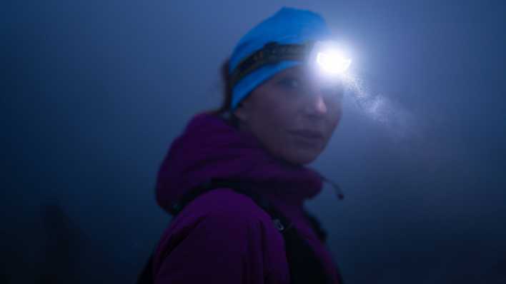 Eine Wanderin mit Stirnlampe auf einer nächtlichen Bergwanderung.