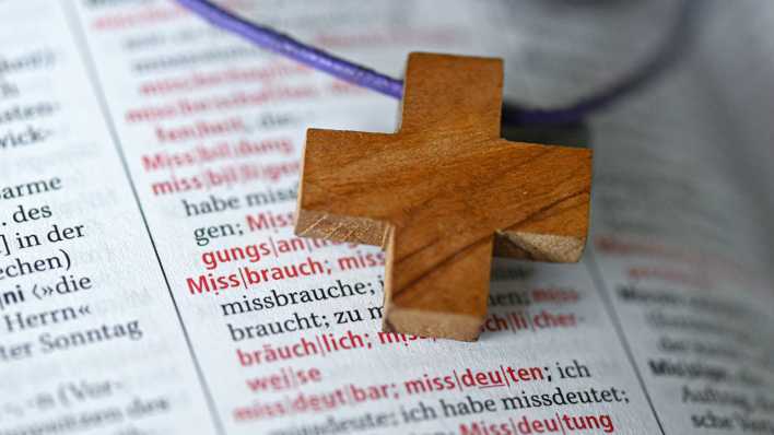 Ein Holzkreuz liegt auf dem Wort "Missbrauch" in einem Duden