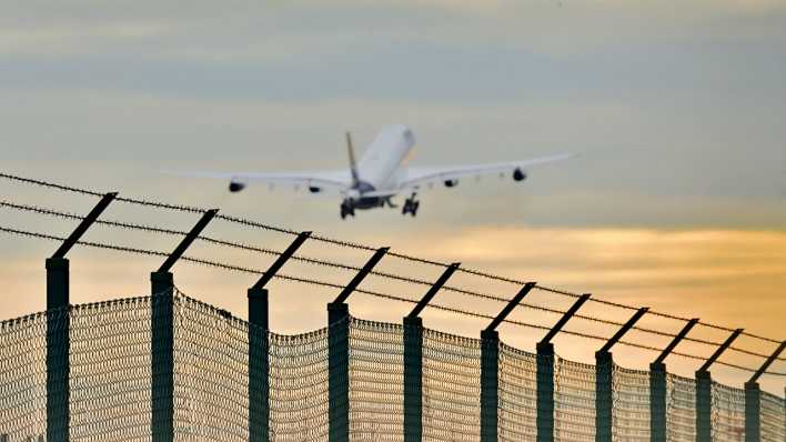 Ein startendes Flugzeug hinter einem Stacheldrahtzaun