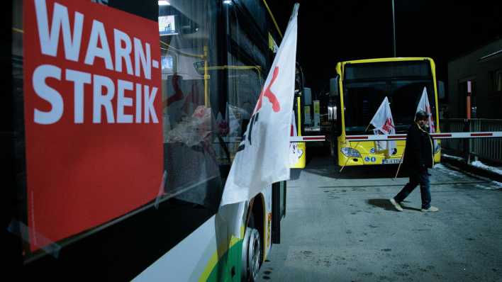 Eine Frau geht an Bussen der Berliner Verkehrsbetriebe BVG mit Fahnen der Gewerkschaft Verdi und dem Schild "Heute Warnstreik" im Betriebshof Lichtenberg entlang (Bild: picture alliance/dpa/Carsten Koall)