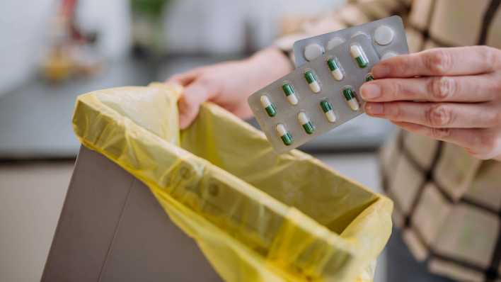 Eine Frau wirft mehrere Medikamenten-Packungen in den Mülleimer.