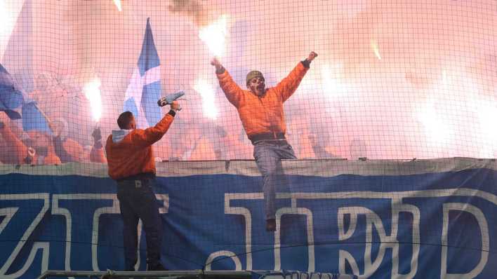 Ein vermummter Fan des FC Hansa Rostock mit einer Pyrofackel in der Hand.