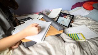 Eine Schülerin arbeitet in ihrem Bett mit einer Freundin per Videochat zusammen.