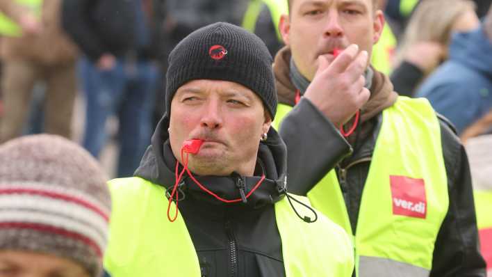 Teilnehmer einer Verdi-Demonstration pfeifen auf Trillerpfeifen.