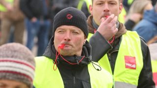 Teilnehmer einer Verdi-Demonstration pfeifen auf Trillerpfeifen.